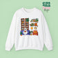 White  Gildan Crewneck Sweatshirt Featuring a Graphic design featuring a cute ghost with a floral bow reading on a purple couch surrounded by cute house plants and 2 bookcases and shelves with books